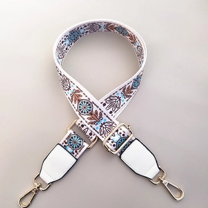 Detail of adjustable embroidered floral bag strap with gold metal hooks and PU leather ends