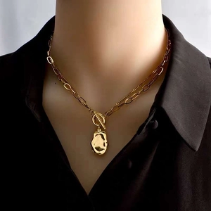 Detail of layered gold OT buckle necklace with lava-textured oval pendant on black shirt