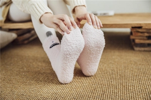 Close-up of pink coral fleece socks featuring cartoon faces and plush ball decorations