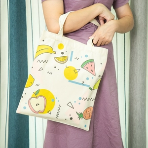 Detail van een crème canvas tas met kleurrijke fruitillustraties en geometrische patronen