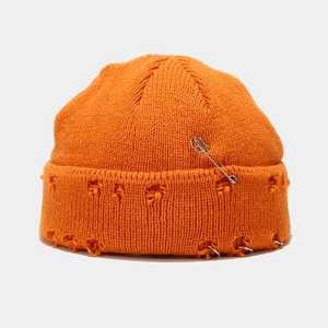 Detailansicht der orangefarbenen Strickmütze mit Distressed-Löchern und silbernen Metallringen