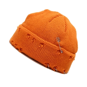 Kaputte orangefarbene Strickmütze mit silbernen Ringen und Sicherheitsnadeln im Streetstyle