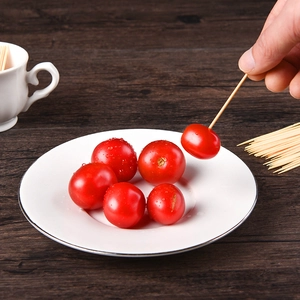 Disposable bamboo toothpicks used for picking up cherry tomatoes on a wooden table