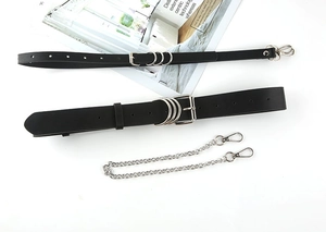 Flat lay of black PU leather belts with silver metal chains and decorative chains on white