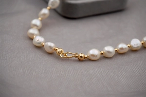 Close-up of baroque pearl necklace featuring a detailed gold toggle clasp on soft fabric