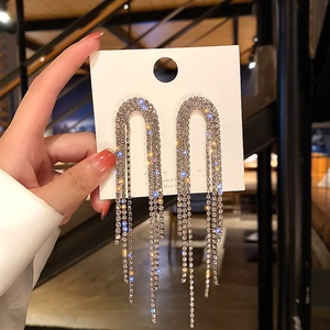 Macro detail of U-shaped silver long tassel earrings with sparkling rhinestones inlay