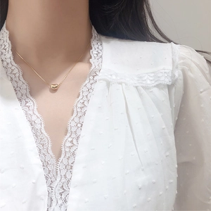 Close-up of a gold bean pendant necklace on a model wearing white lace clothing