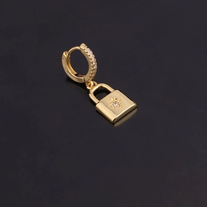 Détail macro d'une boucle d'oreille en or avec pendentif cadenas en zircone sur fond noir