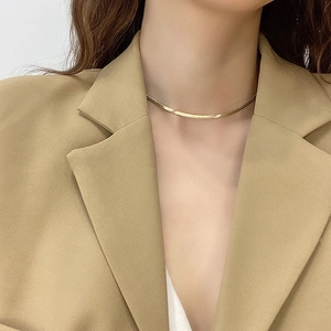Detailed view of a sleek gold snake chain necklace on a model wearing a beige blazer