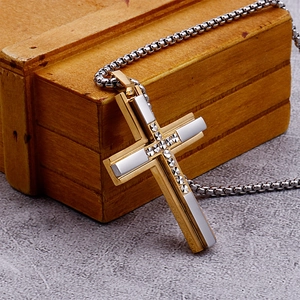Detailed view of dual-tone gold and silver cross pendant on a textured wooden surface