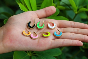 Close-up of vibrant C-shaped enamel hoops with inlaid crystals held in hand for scale