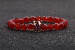 Detailed macro shot of red faceted beads and a rose gold crown charm on a bracelet