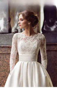 Detailed view of white long-sleeve lace embroidery and satin bodice of bridal gown