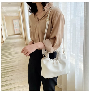Detail of white pleated shoulder bag with metal hook and adjustable slim leather strap