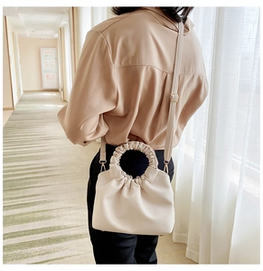 Chic beige ruched crossbody bag with unique round handle shown on model in modern interior
