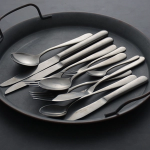 Vintage stainless steel flatware set with matte finish on a dark metal tray