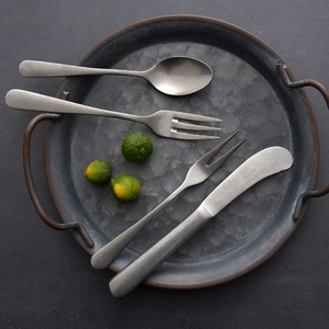 Vintage stainless steel cutlery set with matte finish on a rustic metal tray with limes
