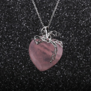 Collier avec pendentif cœur rose et nœud argenté sur un fond étincelant brillant