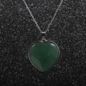Detail view of a heart-shaped green stone pendant with a polished silver necklace chain