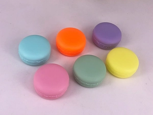 Top view of six colorful macaron-shaped cosmetic jars for cream and lip balm storage