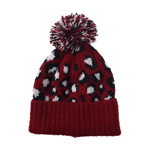 Detail of red leopard print knit beanie featuring a fluffy tricolor faux fur pompom top
