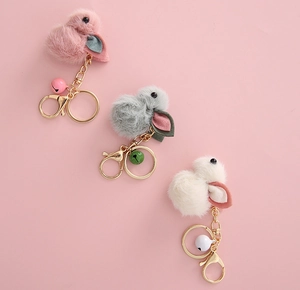 Close-up of three plush bunny keychains in pink, grey, and white with matching bells