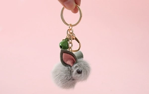 Close-up of a grey plush rabbit keychain with a green bell and golden ring