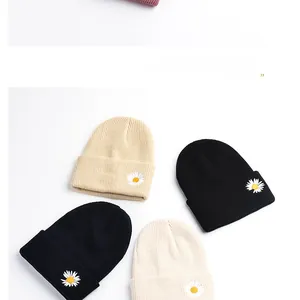 Detail of four ribbed knit beanies in neutral colors with daisy embroidery accents