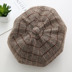 Top view of brown plaid woolen newsboy cap with Kinfolk magazine on white desk