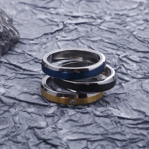 Vertical stack of three slim stainless steel rings in blue, black, and gold with a small diamond