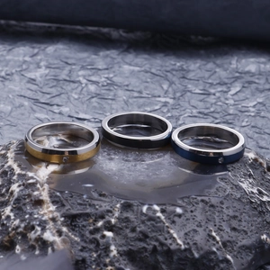 Detail of three brushed stainless steel rings with inset stones on dark grey stone surface