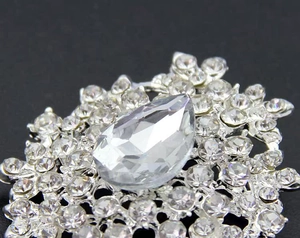 Macro detail of tear-drop crystal brooch featuring small round stones on silver base