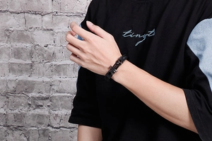 Close-up of men's black braided leather bracelet featuring a silver metal cross charm