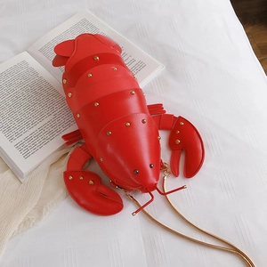Macro shot of creative red lobster-shaped crossbody bag with golden studs on a book