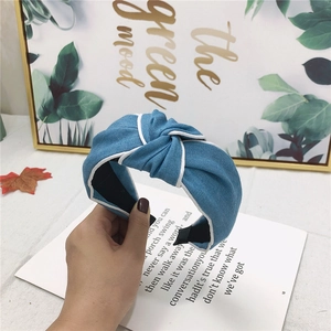 Blue denim knotted headband with white piping detail held against a stylish background
