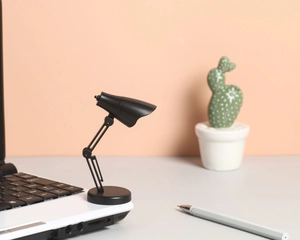 Mini lampe LED noire orientable avec articulations posée sur un bureau avec un cactus