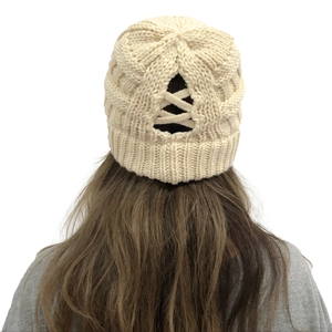 Detail of beige cable knit beanie with messy bun ponytail cross-back opening