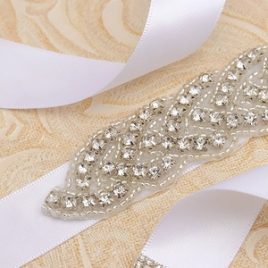 Close-up of elegant crystal leaf applique with silver beads on white satin ribbon belt