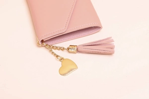 Detailed close-up of pink leather wallet with gold heart pendant and soft fringe tassel