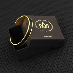 Close-up of a gold C-shaped cuff bracelet with black leather inlay on a gift box