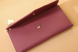 Detail of wine red faux leather wallet featuring a gold heart charm and magnetic closure