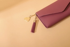 Close-up of pink PU leather wallet with gold heart pendant and matching tassel detail