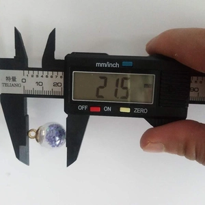 Digital caliper measuring the 21.5mm diameter of a purple dried flower glass ball charm