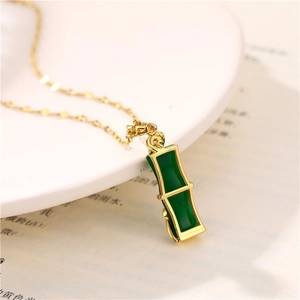 Collana con pendente in bambù dorato e giada verde su sfondo di un libro vintage