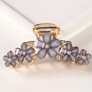 Macro shot of gold metal hair claw clip featuring five purple cat-eye flowers and rhinestones