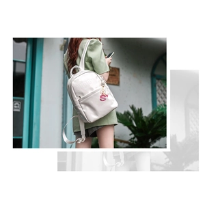 Detail showing white patent leather backpack texture with embossed lettering and pink charm