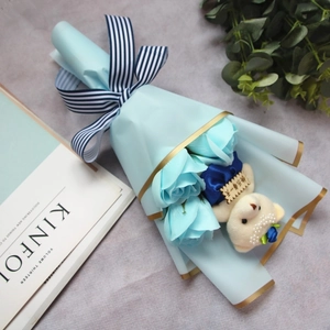 Close-up of blue soap flower bouquet with cream teddy bear and striped ribbon gift box