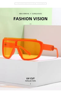 Close-up of orange fashion sunglasses with gold hexagon temple detail on white pedestal