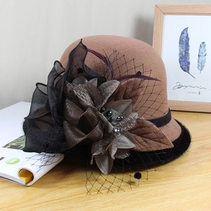 Detail of wool cloche hat with black silk flower, feathers, and mesh veil on wooden desk