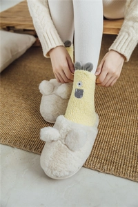 Detail of cute yellow cartoon monster socks worn with plush slippers on a woven rug